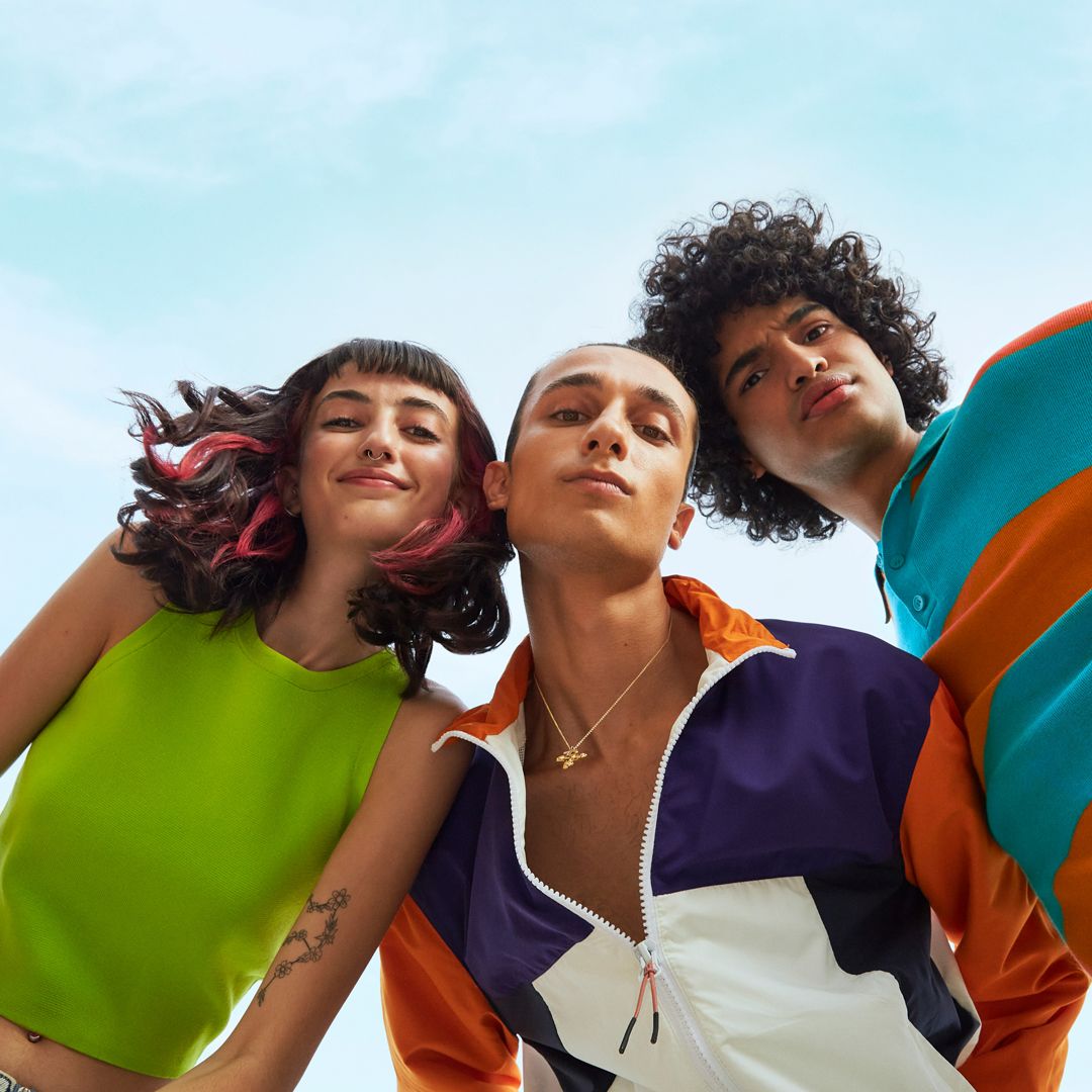 Three Gen Z young adults in bold, colorful clothing photographed from below against a blue sky—expressing confident, vibrant personal style