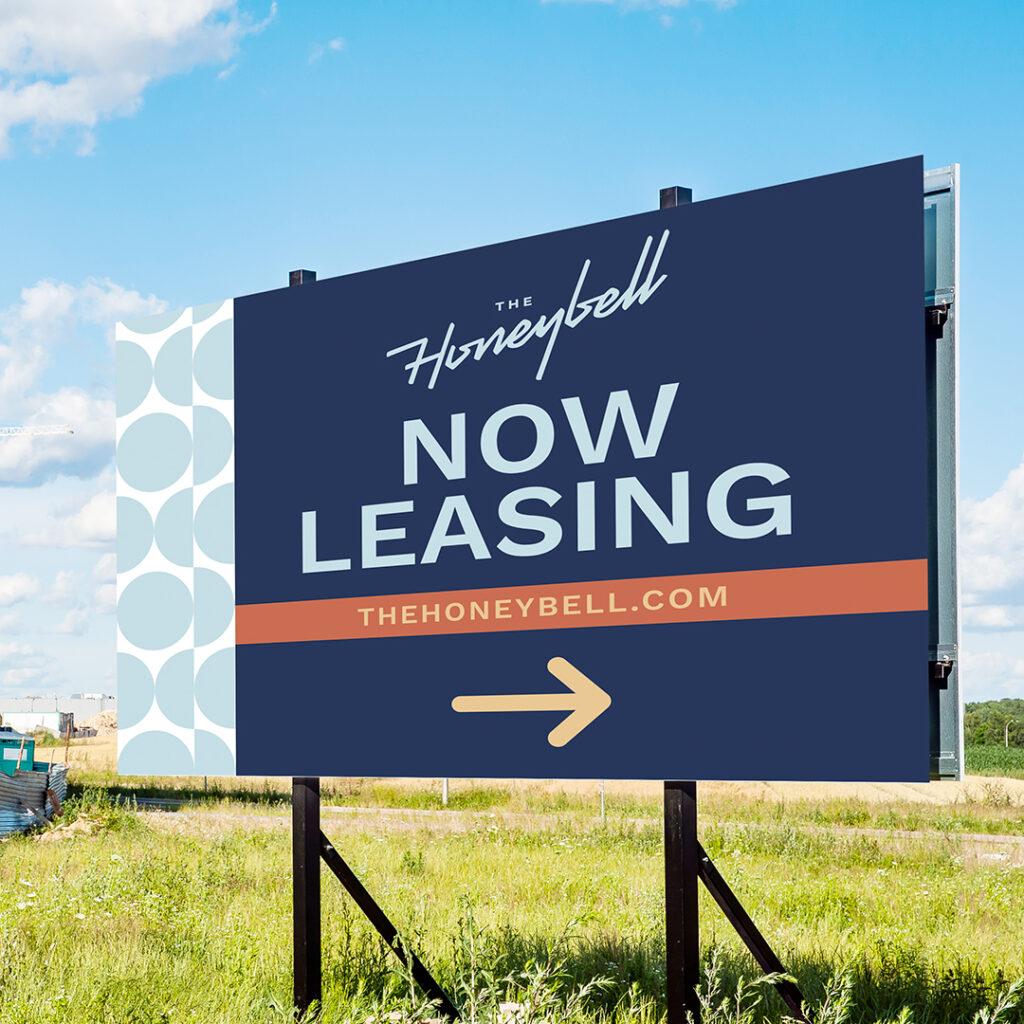 The Honeybell large outdoor branded yard sign displaying Now Leasing with navy blue background and directional arrow showing consistent apartment brand identity